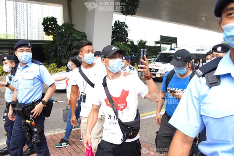 【警察與白衣人搭膊頭 白衣人在警察背後舉中指】